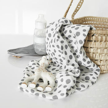 Dalmation print baby muslin swaddle cloth rolled up on a white background next to real bamboo shoots