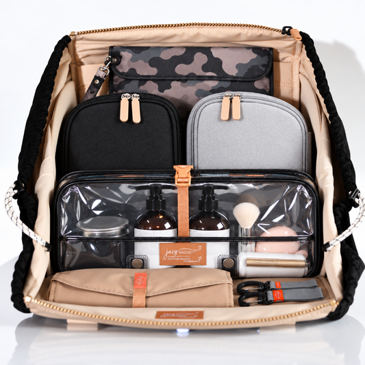 An open beige and black backpack organizer filled with travel and makeup accessories, including a camouflage pouch, black and gray zip cases, clear plastic toiletry bags, bottles, brushes, and a beige pouch, photographed on a clean white background.