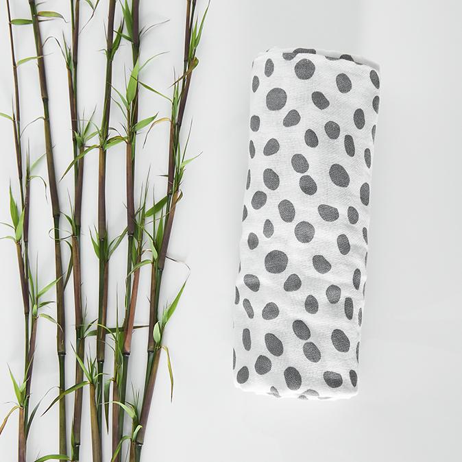 Dalmation print baby muslin swaddle cloth rolled up on a white background next to real bamboo shoots