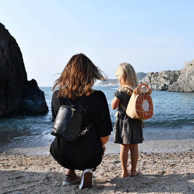 Woman kneeling on a beach wearing a freedom podwith her child wearing a toddler pod backpack 