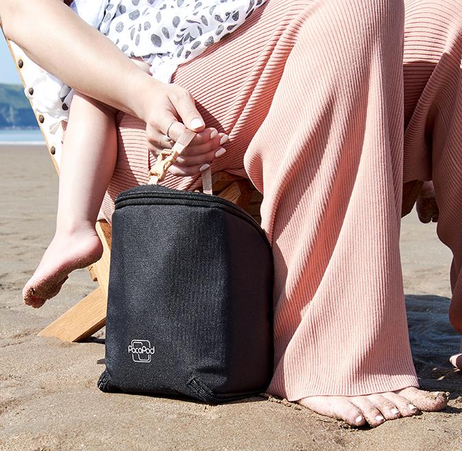 Woman sitting on a beach with a toddler with the Feeder Pod black beside her