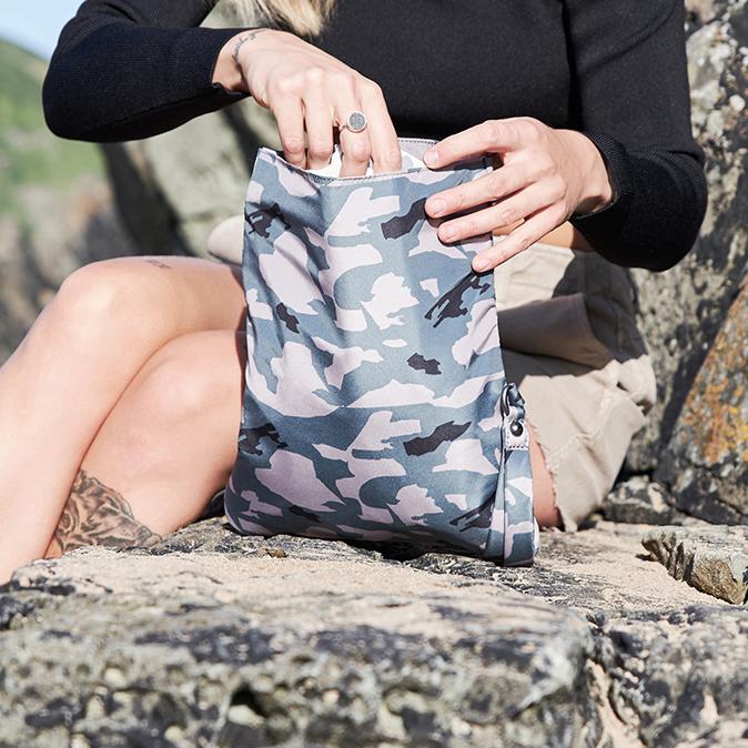 Woman on some rocks tucking an items into the pacadry bag camo