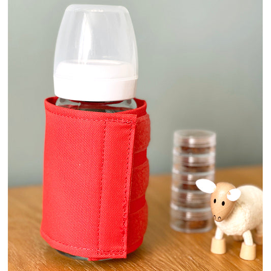Lifestyle image of the black thermal bottle wrap around a bottle with a wooden sheep toy next to it