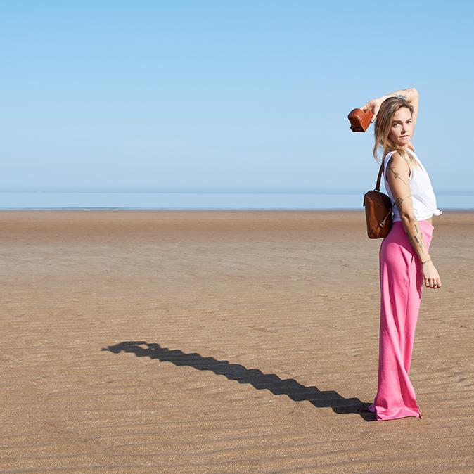 Woman on the beach wearing the freedom pod backpack and holding a tan camera case over her head