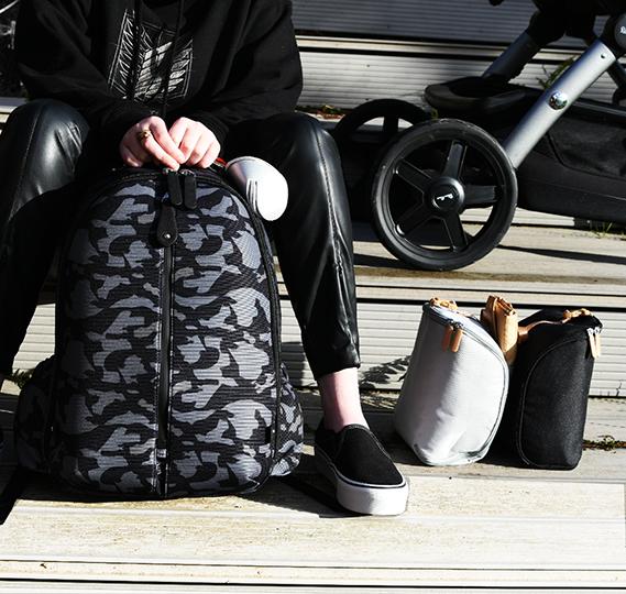 Woman sat in sunshine next to a pushchair with her hands on a Picos Calo backpack and the pods on the floor beside her